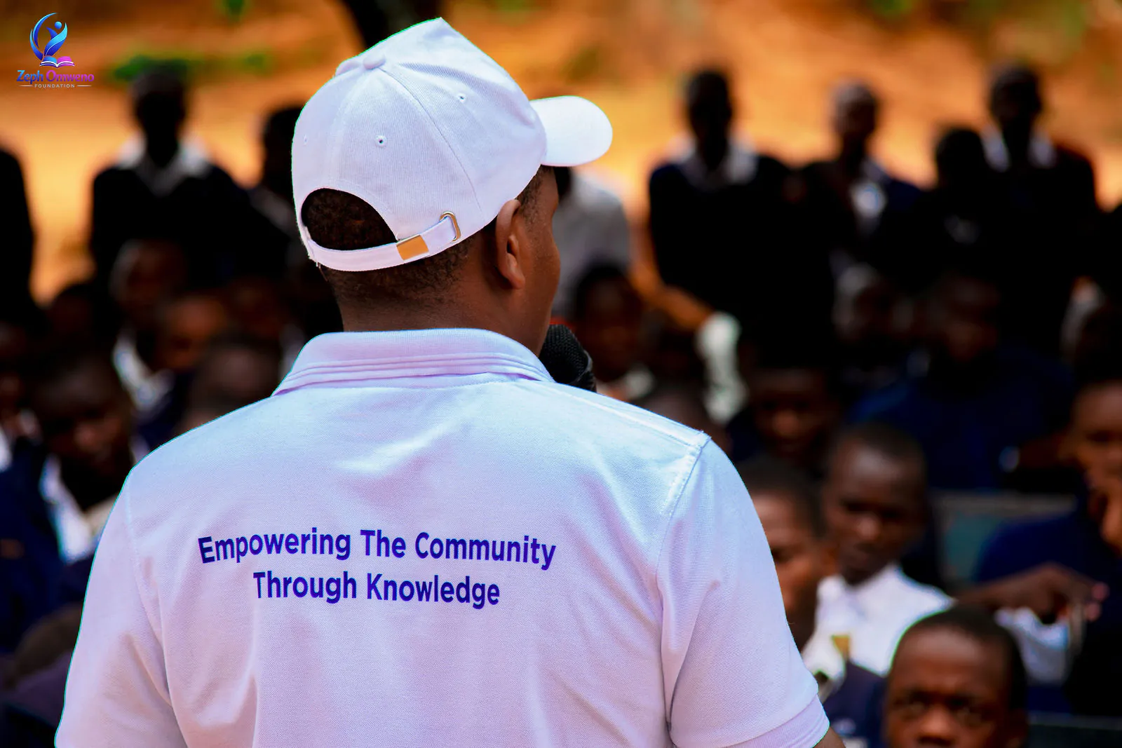 A ZOF mentor in an 'Empowering the Community Through Knowledge' shirt addressing students